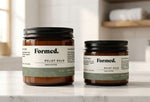 Two jars of Formed Relief Balm on a marble surface with a neutral background.